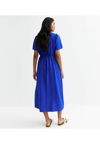 Vestido azul de longitud hasta la rodilla con mangas cortas abullonadas y cintura ceñida. Tejido suave que cae hasta la mitad de la pantorrilla, combinado con sandalias color tostado.