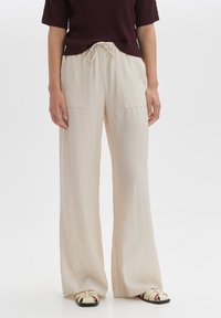 Lichtbeige wijde broek met twee voorkezen en een trekkoord in de taille, gemaakt van een zachte textuur. Gecombineerd met zwarte spiked sandalen.