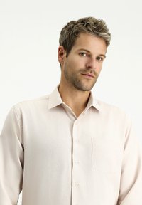 Camicia button-up a maniche lunghe di color beige chiaro con taschino, caratterizzata da una texture sottile e un design con colletto classico.