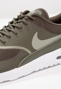 Nike tenisky v olivově zelené barvě, vyrobené z prodyšné síťoviny a syntetických materiálů, s šněrováním a bílou mezipodešví s viditelnou vzduchovou jednotkou.