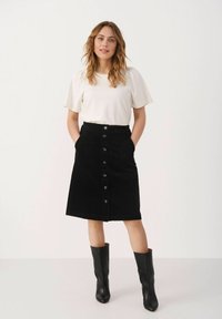 Black corduroy skirt with front buttons, side pockets, knee-length. Paired with a plain white short-sleeve top and black knee-high boots.