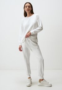 Witte katoenen sweatshirt met lange mouwen, ontspannen pasvorm. Gepaard met witte taps toelopende joggingbroek met een trekkoord in de taille en zijaccenten. Witte sneakers.