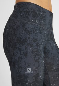 Högmidjade svarta leggings med ett texturerat, mönstrat tyg i nyanser av mörkgrått och subtila accenter. Logotypen är placerad på underbenet.