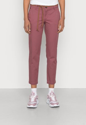 Persoon draagt korte mauve broek met een bruine gevlochten riem en roze-witte FILA sneakers met witte sokken.
