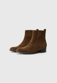 Bottines en suède marron avec une texture lisse, un bout rond, un petit talon empilé et des languettes de traction. Présente un design simple et élégant.