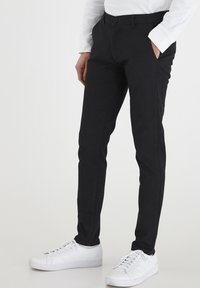 Svarta skräddarsydda långbyxor med smal passform, knappstängning och sidofickor, kombinerade med vita sneakers. Slät tyg och rena linjer.