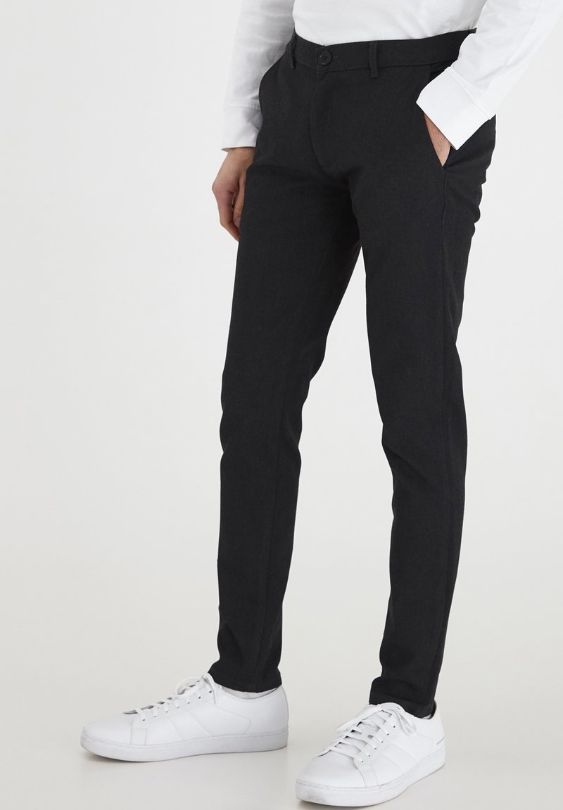 Svarta skräddarsydda långbyxor med smal passform, knappstängning och sidofickor, kombinerade med vita sneakers. Slät tyg och rena linjer.