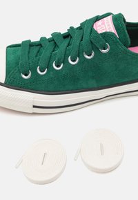 Gröna mockasko med vit gummitå och svart rand. Inkluderar två rund vita snören med plastspetsar. Rosa insidan accent.