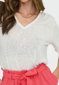 Witte, los vallende, lichte V-hals shirt gecombineerd met een hoogstaande roze rok met een gerimpelde tailleband en een strikdetail.