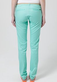 Pantalons vert menthe à coupe slim, en tissu lisse, avec une taille texturée et des poches arrière. Sa couleur de base renforce la polyvalence.
