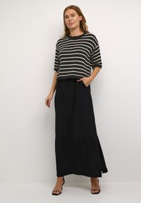 Top in maglia a righe nero e crema, maniche corte. Gonna maxi nera fluida con tasche, con uno spacco laterale. Sandali con tacco.
