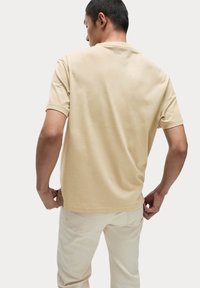 T-shirt in cotone beige con maniche corte, scollatura rotonda e una vestibilità comoda. Design semplice senza motivi o dettagli.