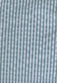Textiel met verticale strepen in zacht groen en wit, met een textuur die een lichte glans heeft, netjes afgewerkt met stiksels aan de onderkant.