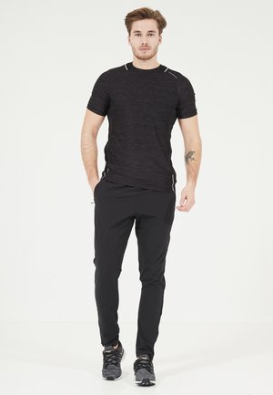 Sort atletisk T-shirt med korte ærmer, struktureret stof og reflekterende detaljer, parret med sorte tapered bukser og mønstrede løbesko.