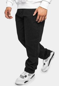 Pantaloni in denim neri con un design a gamba dritta. Indossati con sneaker bianche con dettagli neri e una superficie texturizzata.