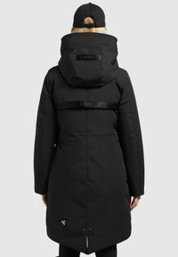 Parka nera impermeabile con cappuccio, caratterizzata da un design con vita arricciata, fessure laterali e dettagli con strap di marca sulla schiena.
