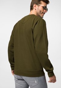 Oliwkowy sweter z okrągłym dekoltem, luźnym krojem i żeberkowymi mankietami; charakteryzuje się gładką fakturą i subtelnym detalem szycia.