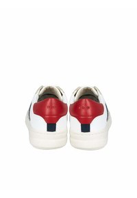 Zapatilla blanca con un acento rojo en el talón, rayas en azul marino y una superficie texturizada. El material parece suave con un diseño de perfil bajo.