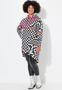 Hoodie-tunic in zwart-wit ruitpatroon, met roze en oranje sterren, een gebogen zoom en lange mouwen. Gecombineerd met glanzende leggings.