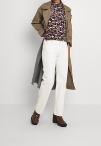 Brun trenchcoat över en marinblå blommig långärmad topp, vita jeans och bruna platåskor; har en avslappnad passform och släta texturer.