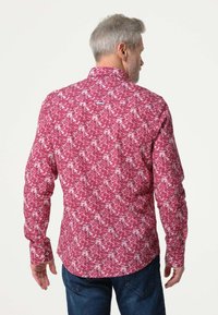 Rood en wit langemouwen shirt met een bloemenpatroon, met knopenkraag en een gebogen zoom. Materiaal lijkt glad en heeft een lichte textuur.