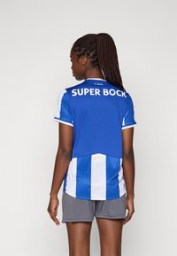 Modrá a biela futbalová dres s brandingom "SUPER BOCK" a FC Porto, krátke rukávy a ľahký materiál. Na spodnej strane sú viditeľné šedé šortky.