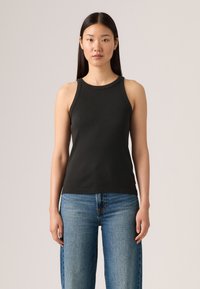 Svart ribbet tanktopp med rund hals og brede stropper, kombinert med lys blå vide jeans. Glatt tekstur, uformell design.