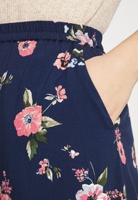 Pantalons floraux avec un fond marine, ornés de fleurs roses et bleues, dotés d'une ceinture élastique et de poches latérales pour un usage pratique.