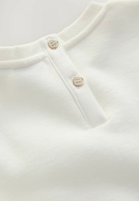 Sweatshirt blanc avec un col côtelé, doté de trois petits boutons clairs et d'une texture douce. Design simple avec une finition soignée.