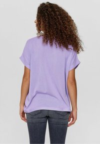 Lavendelfärgad kortärmad topp med en avslappnad passform. Har en mjuk textur och en rak nederkant, kombinerad med mörkgrå tajta jeans.