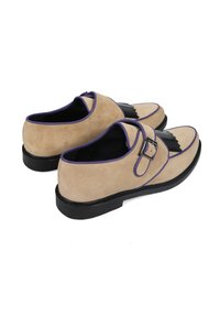 Beżowe zamszowe buty z fioletowymi akcentami, klamrą i czarnym dekoracyjnym frędzlem. Gruba czarna podeszwa z zaokrąglonym czubkiem.