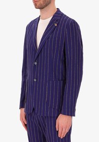 Blazer a righe blu navy realizzato in tessuto testurizzato, caratterizzato da chiusura a due bottoni, revers a freccia e taschino sul petto con spilla decorativa.