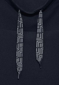 Marinblå hoodie i texturerat tyg, med mönstrade dragsko i svart och vitt geometriskt mönster. Inkluderar metallspetsar på dragskorna.