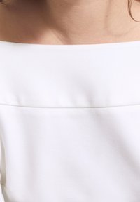 Weißes schulterfreies Oberteil mit glatter Textur und minimalistischem Design. Verfügt über einen sauberen Ausschnitt und subtile Nahtdetails.