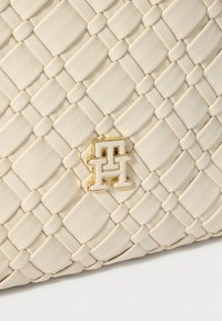 Krēmkrāsas austā ādas rokassoma ar zeltīta toņa logotipa akcentu. Raksts ar kvadrātveida un taisnstūrveida formām. Gluda apdare.