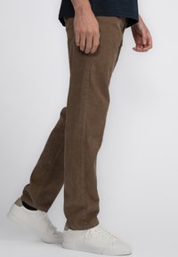 Bruine corduroy broek met een rechte pasvorm, voorzien van subtiele verticale ribbeling, gecombineerd met witte sneakers.