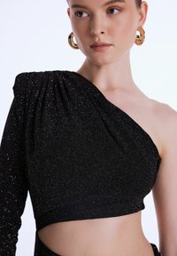 Černý top na jedno rameno s třpytivou texturou, s nabíraným detailem na levé straně a výřezem na pravé straně. Jednoduchý design, přiléhavý střih.