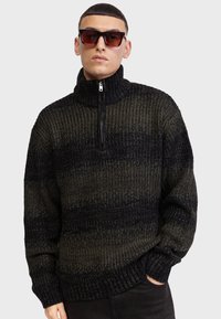 Pull en maille avec col haut, demi-zip, et un motif dégradé allant du vert foncé au noir. Fabriqué avec un fil texturé.