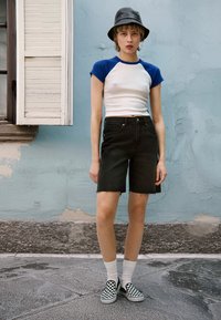Camicetta bianca a maniche corte con maniche blu, pantaloni shorts in denim neri e scarpe slip-on a scacchi bianco e nero. Stile aderente, look informale.