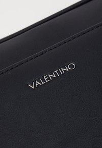 Pouch din piele neagră, cu cusături vizibile și un logo argintiu în relief "Valentino" pe față, având o textură netedă și un design elegant.