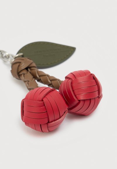 Μπρελόκ με δύο πλεγμένες κόκκινες δερμάτινες μπάλες, που είναι προσαρτημένες σε καφέ πλεγμένα δερμάτινα στελέχη και μια πράσινη δερμάτινη ετικέτα σε σχήμα φύλλου σε λευκό φόντο.