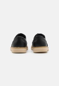 Scarpe in pelle nera con superficie testurizzata, punta arrotondata e suola in gomma beige, con dettagli perforati lungo i lati.