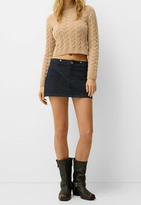 Béžový svetr s copánkovým vzorem a krátkým střihem, tmavě modrá mini sukně z denimu a černé kozačky po kolena s přezkami a cvočky. Jednoduchý a ležérní outfit.