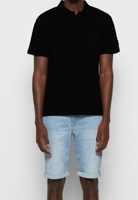 Czarna koszulka polo wykonana z bawełny, z trzema guzikami przy kołnierzyku, krótkimi rękawami, zestawiona z jasnoniebieskimi krótkimi spodniami dżinsowymi z podwiniętymi mankietami.