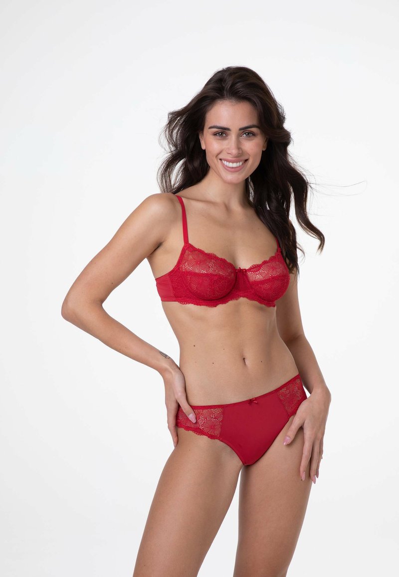 Reggiseno rosso in pizzo con ferretto e spalline regolabili, abbinato a slip con bordatura in pizzo e un fiocco decorativo sul davanti.