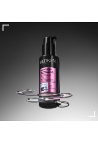 Redken Naked Gloss, lekki olejek nabłyszczający w czarnej butelce z różową etykietą. Posiada pompkę oraz przezroczyste krople wokół podstawy.