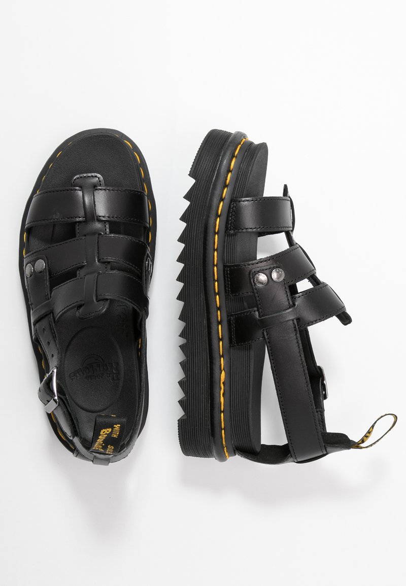 Las sandalias de cuero negro presentan un diseño de tiras con hebilla ajustable y suela de zig zag. Un notable pespunte amarillo acentúa los lados.