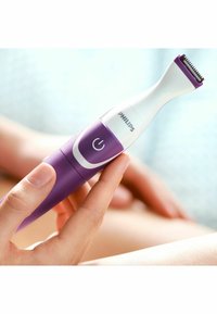 Tondeuse Philips avec un design blanc et violet, forme ergonomique, tête de lame en métal et bouton marche/arrêt. À main, tenue près de la peau.
