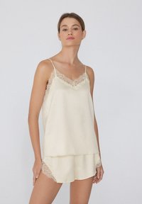 Pyjama beige soyeux avec bordure en dentelle ; le débardeur possède des bretelles ajustables, tandis que le short présente des accents en dentelle le long de l'ourlet.