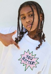 Hvid bomulds t-shirt med en pailletpræget grafik i livlige farver med teksten "DU BETYDER NOGET!" i et stjerneskud design.